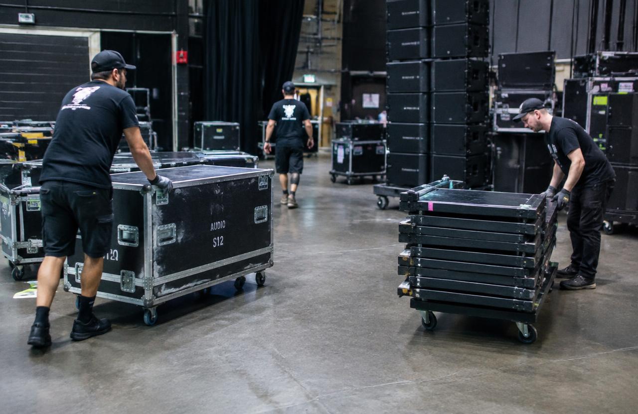 Production crew rolling audio road cases and stacked stage deck panels at a venue